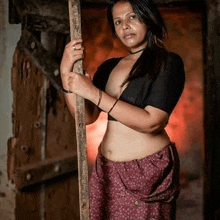 a woman in a crop top and purple skirt is standing next to a wooden post .