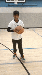 a boy in a white shirt with the letter r on it is holding a basketball on a basketball court .