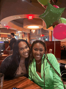 two women are posing for a picture in front of a red exit sign