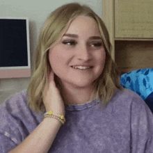 a woman in a purple shirt is smiling and touching her hair while sitting in front of a computer .