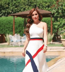 a woman in a white pleated dress stands in front of a pool