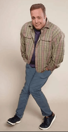 a man wearing a plaid shirt and blue pants is standing with his hands in his pockets .
