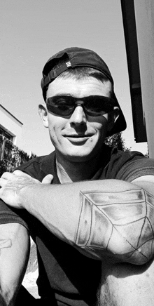 a man wearing sunglasses and a baseball cap has a tattoo on his arm