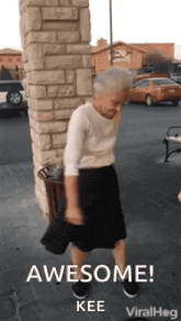 an elderly woman is dancing in front of a brick wall and a trash can .