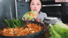 a woman is eating a wrap of lettuce in front of a pot of food and a sign that says keemikim