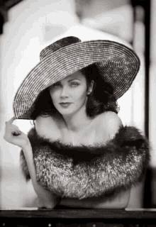 a black and white photo of a woman wearing a hat and fur .