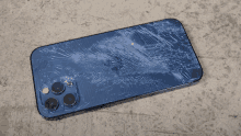 a blue iphone with a cracked screen is laying on a concrete surface