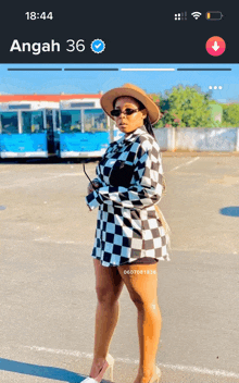 a woman wearing a checkered shirt and a hat is standing in a parking lot with the time of 18:44