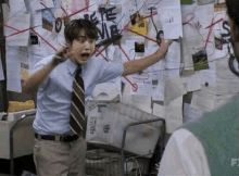 a man in a blue shirt and tie is standing in front of a bulletin board with papers on it .