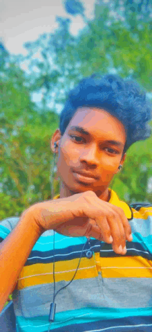 a young man wearing ear buds and a striped shirt looks at the camera