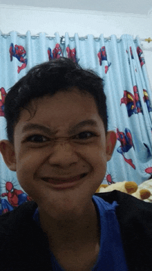 a young boy making a funny face in front of a curtain with spider-man on it