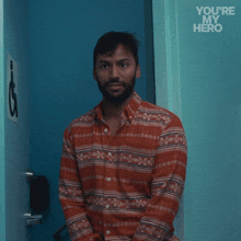 a man in a striped shirt stands in front of a blue door with the words " you 're my hero " written on it