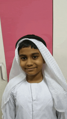 a young boy wearing a white scarf around his head smiles for the camera