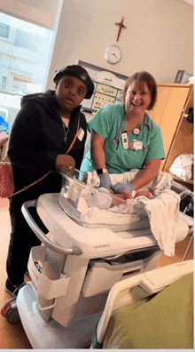 a woman in a hospital room with a nurse and a baby in a crib