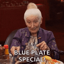 an elderly woman is sitting at a table with a plate of food and the words " blue plate special " above her