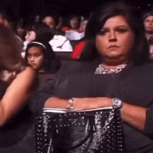 a woman is sitting in a crowd with her arms crossed and holding a purse .