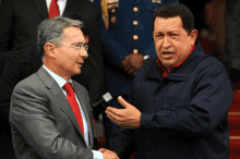 a man in a suit and red tie talks to another man in a blue jacket