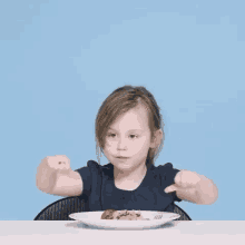 a little girl is sitting at a table with a plate of food and making a thumbs up sign .