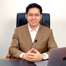 a man in a suit sits at a desk with a laptop