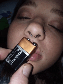 a woman holds a duracell battery in front of her nose