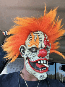 a man wearing a clown mask with orange hair smoking a cigarette