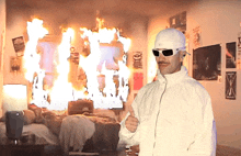 a man giving a thumbs up in front of a room that is on fire