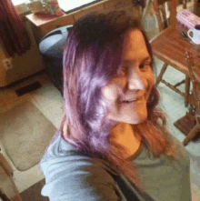 a woman with purple hair is taking a selfie in a kitchen while smiling .