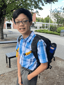 a young man wearing glasses and a blue plaid shirt is carrying a black backpack