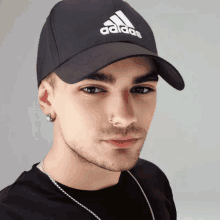 a man wearing a black adidas hat and a silver chain around his neck