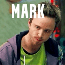 a man wearing a green shirt and a purple hoodie with the word mark written on his forehead .