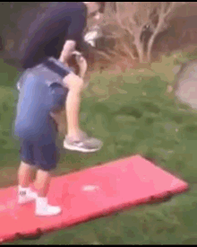 a little boy is standing on a red mat while a man holds his leg over his head .