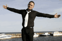 a man in a black shirt and tie is standing in front of boats .