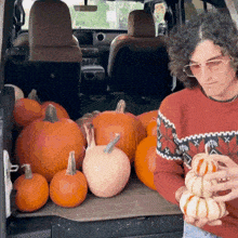 a man in a red sweater is holding a pumpkin in front of pumpkins in the back of a car