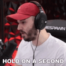 a man wearing headphones and a red hat says " hold on a second "