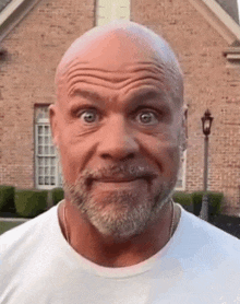 a bald man with a beard and mustache is making a funny face in front of a brick house .