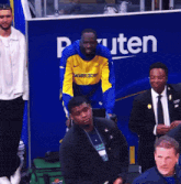 a man in a warriors jacket stands in front of a blue wall