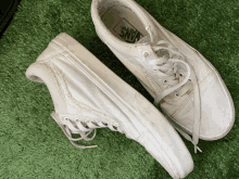 a pair of white vans shoes are sitting on a green surface