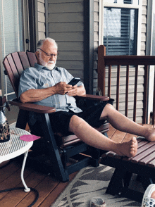 an elderly man sits in a chair on a porch looking at his phone