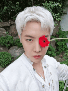 a person with white hair is holding a red flower to their eye