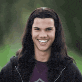 a young man with long dark hair is smiling and wearing a black hoodie