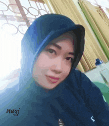 a woman wearing a blue hijab has the name nugi written on the bottom