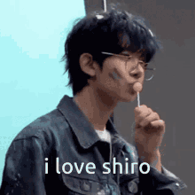 a young man wearing glasses is holding a lollipop in his mouth and says `` i love shiro '' .