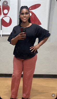 a woman in a black top and pink pants takes a picture of herself in a mirror