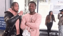 two men are standing next to each other with their arms crossed in front of a bus stop .