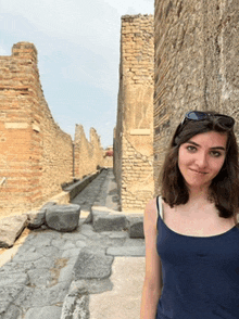 a woman in a blue tank top is standing in front of a stone wall