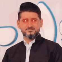 a man with a beard and red eyes is wearing a black jacket and a white shirt .