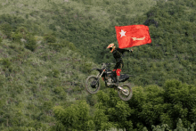 a man on a dirt bike is flying through the air while holding a flag with a star on it