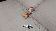 a stuffed mickey mouse is laying on a bed with the word cap above it