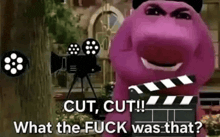 barney from sesame street is holding a clapper board in front of a movie camera .