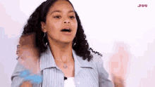 a young girl with curly hair is standing in front of a white wall and making a funny face .